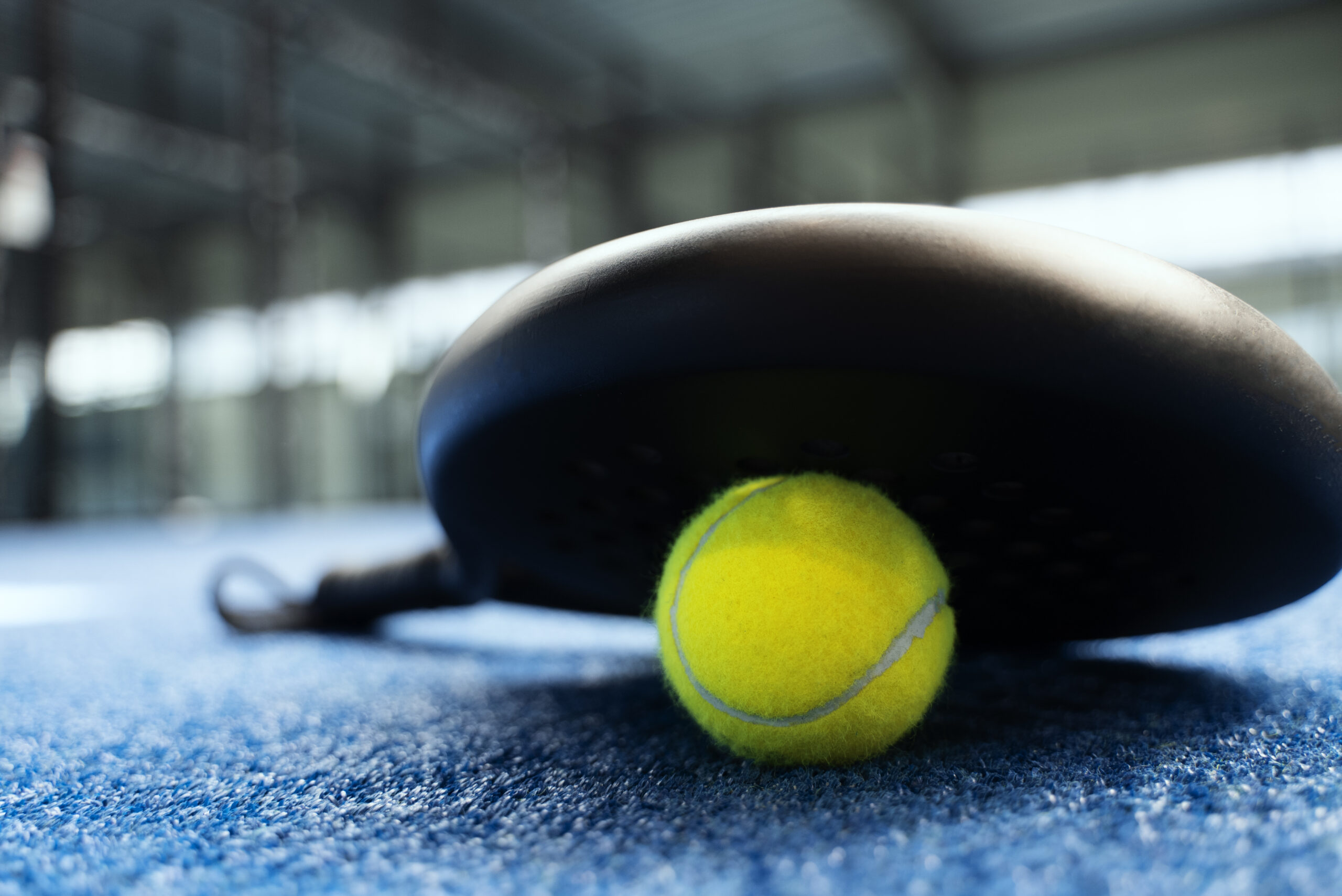 A padel racket and ball close-up on court
